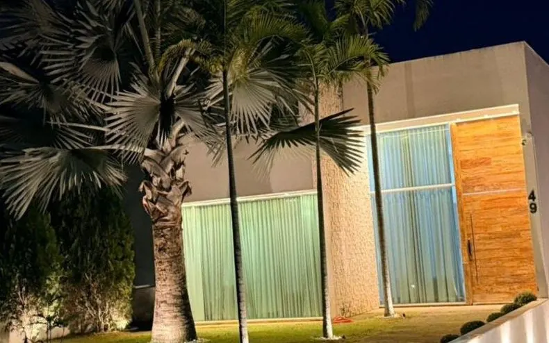 Fachada de casa com palmeiras e jardim iluminados à noite